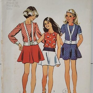 May include: A vintage Simplicity sewing pattern for girls' dresses. The pattern number is 6189 and the price is $1.00. The pattern is for stretch knits only. The pattern includes three different dress styles. The first dress is a red and white polka dot dress with a white cardigan. The second dress is a white dress with a floral print and a blue cardigan. The third dress is a blue and white polka dot dress with a white cardigan.