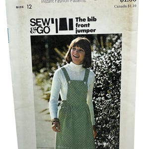 Op de afbeelding: Vintage Butterick naaipatroon voor een tuinbroek met voorkant, maat 12. Het patroon toont een vrouw die een groen patroon tuinbroek draagt over een witte coltrui. Het patroon bevat de tekst "SEW & GO" en "The bib front jumper."