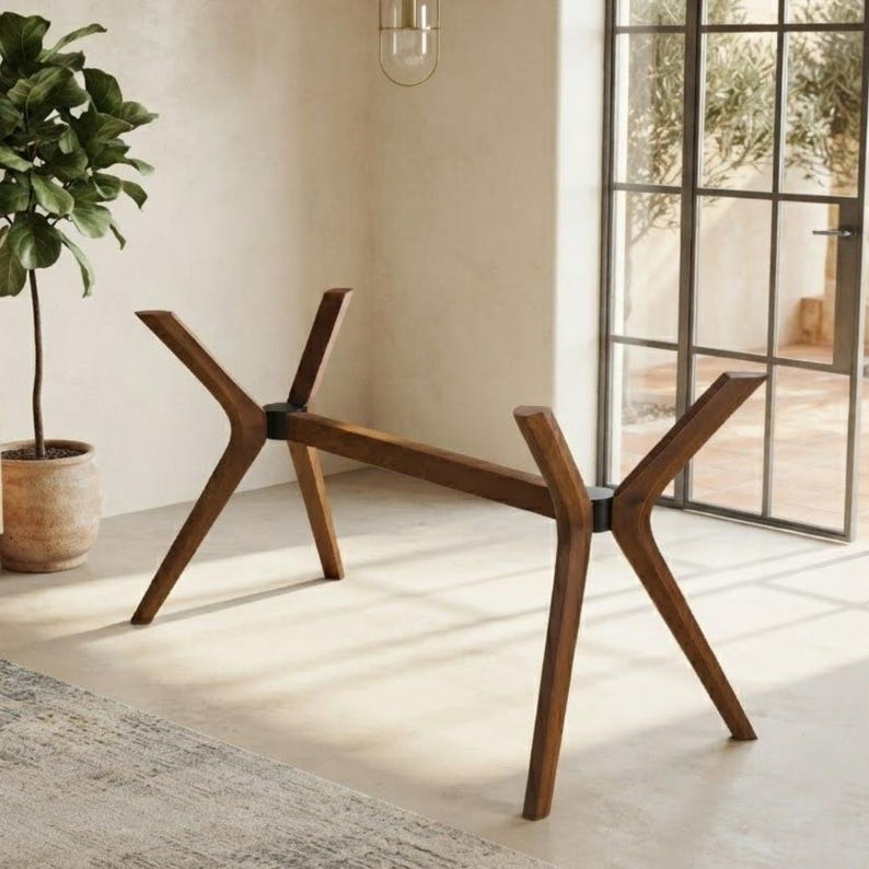 May include: A dark brown wooden table base featuring four angled legs connected by a central horizontal support beam. The structure includes black circular joints where the legs meet the crossbar, creating a stable frame for a tabletop.