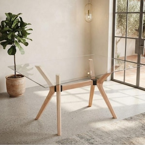 May include: A rectangular dining table featuring a clear glass top supported by a light-toned wooden frame. The base consists of four angled legs connected by black metal joints, providing a stable structure for the transparent tabletop surface.