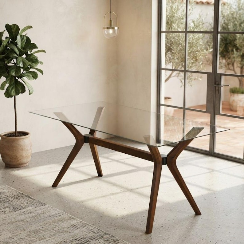 May include: A rectangular dining table featuring a clear glass top supported by a dark brown wooden base with four angled legs that meet at central joints, creating a distinct X-shaped structure at each end of the table frame.