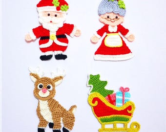 Puede incluir: Cuatro adornos navideños hechos a mano con ganchillo: Papá Noel, Mamá Noel, un reno y un trineo lleno de regalos. Los adornos son rojos, blancos, marrones y verdes, con detalles en negro. Papá Noel y Mamá Noel tienen barbas y pelo blancos.