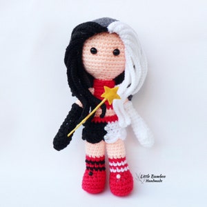 May include: Crocheted doll with black and white hair, wearing a red and black outfit with a star wand. The doll is wearing red and black striped socks and red shoes.