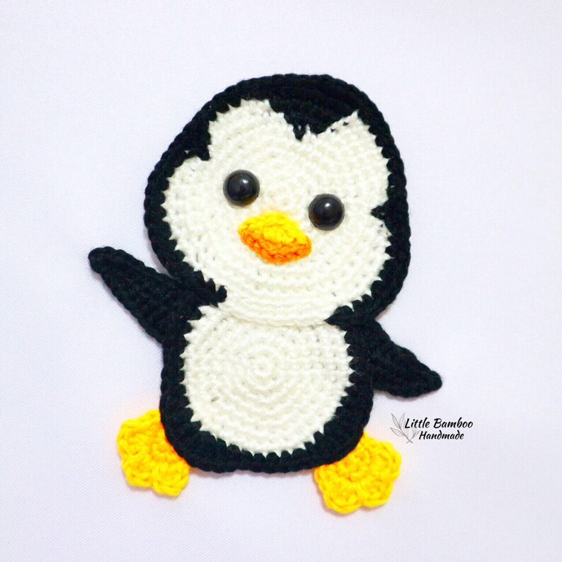 May include: A crocheted penguin with black and white yarn, yellow feet, and black eyes. The penguin is standing on a white background.