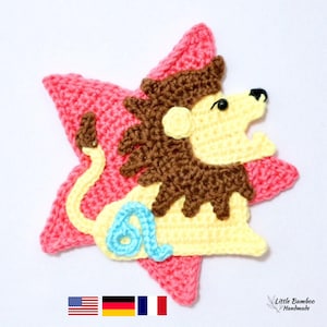 May include: A handmade crochet lion applique in yellow, brown, and blue, set on a pink star. The lion has a detailed mane and a smiling expression. The applique is likely for crafts or decoration.
