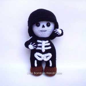 Op de afbeelding: Een handgemaakte gehaakte skeletpop in een zwart jumpsuit met capuchon en witte botdetails. De pop heeft een wit gezicht met zwarte knoopogen en een gestikte mond. De voeten zijn bruin. De tekst "Little Bamboo Handmade" staat onderaan.