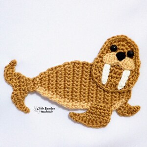 May include: A crocheted walrus with a brown body, white tusks, and black eyes. The walrus is lying on a white surface. "Little Bamboo Handmade" is written below the walrus.