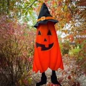 May include: A Halloween decoration shaped like a smiling jack-o'-lantern. The orange pumpkin has a black witch hat with a gold buckle and black legs. The background features fall foliage.