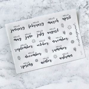 May include: A sheet of stickers featuring the months of the year, seasons, and greetings. The stickers are black and white and include a variety of designs, such as leaves, snowflakes, and suns.