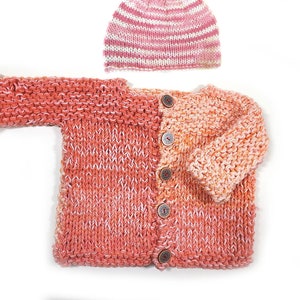 May include: A knitted baby cardigan with a pink and white striped hat. The cardigan is a peachy pink color with a white fleck throughout. The cardigan has a button closure and is made with a soft yarn.