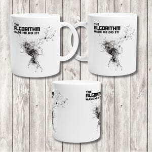 May include: White ceramic coffee mugs with the text "THE ALGORITHM MADE ME DO IT!" and a black and white illustration of a woman's profile with a network design. The mugs are displayed on a light wood surface.