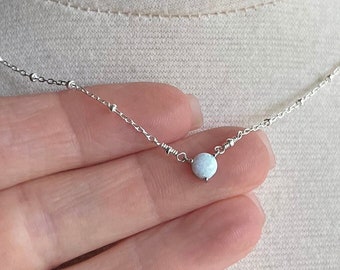 Puede incluir: Un delicado collar de cadena de plata con un pequeño colgante redondo de ópalo blanco.