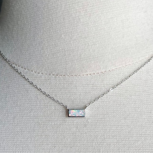 May include: A delicate silver chain necklace with a small rectangular opal pendant. The opal is white with iridescent flashes of color.