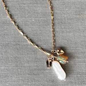 May include: A gold chain necklace with a charm pendant featuring a white pearl, a small gold heart, and a green and brown gemstone.