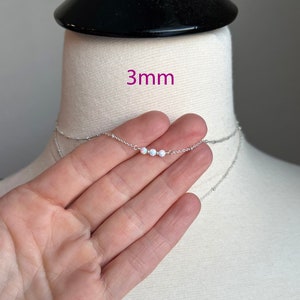 May include: A silver chain necklace with three small white opal beads. The necklace is 3mm wide.