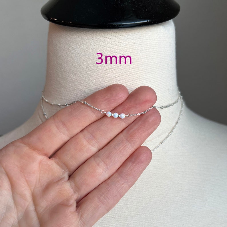 May include: A silver chain necklace with three small white opal beads. The necklace is 3mm wide.