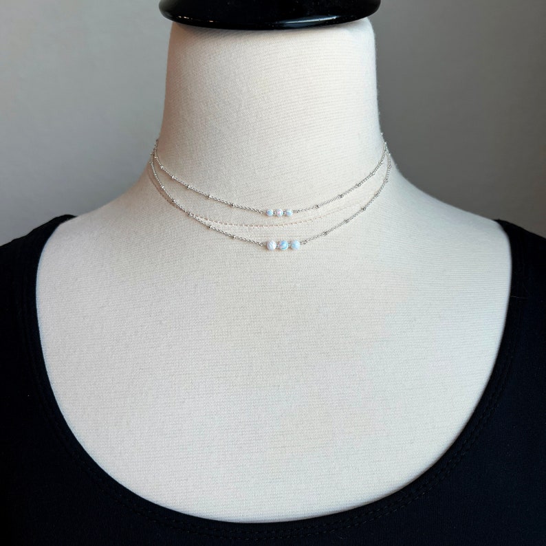 May include: A silver layered choker necklace with three strands of delicate chain and a row of small white opal beads.