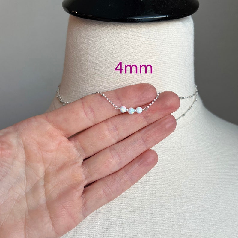 May include: A silver chain necklace with three white opal beads, each measuring 4 mm in diameter. The necklace is displayed on a mannequin's neck.