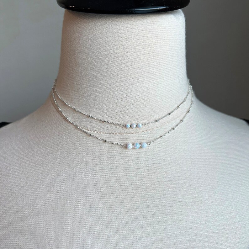 May include: A silver layered necklace with three strands of chain and a row of small white opal beads.