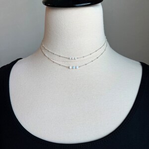 May include: A silver layered necklace with three delicate chains and a row of small white opal beads.