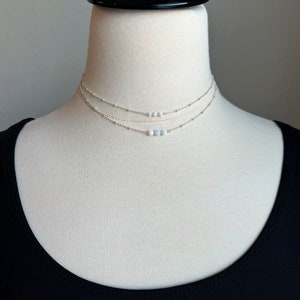 May include: A silver layered necklace with a delicate chain and a row of small white opal beads.