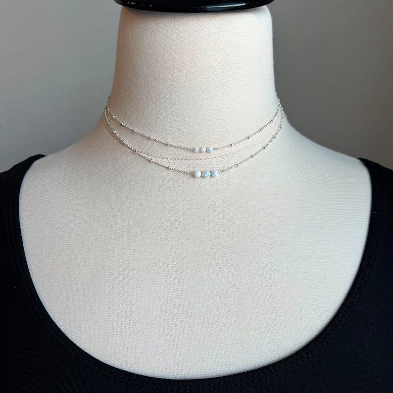 May include: A silver layered necklace with a delicate chain and a row of small white opal beads.
