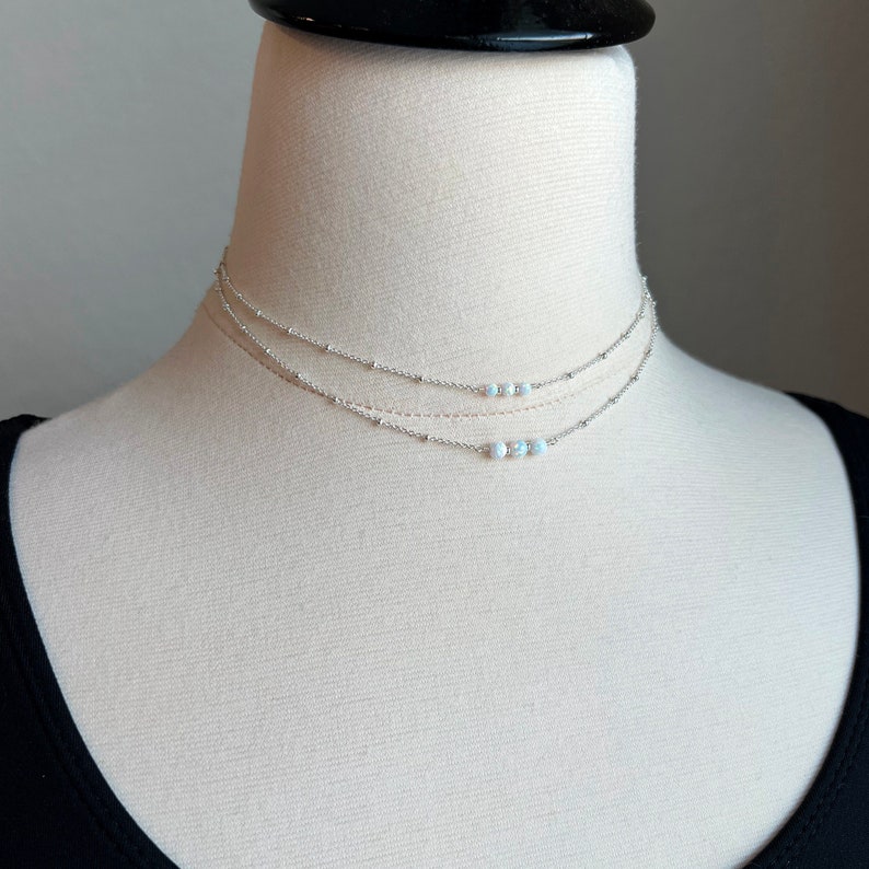 May include: A silver layered necklace with three delicate chains and a row of small white opal beads.