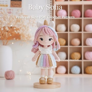 Puede incluir: Muñeca Baby Sofia hecha a ganchillo, con cuerno de unicornio y pelo colorido. Viste un vestido a rayas en colores pastel y zapatos color canela. El texto "Baby Sofia" y "Princess Size PDF Crochet Pattern" es visible.