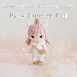 Puede incluir: Una mu&ntilde;eca de beb&eacute; unicornio de crochet con pelo rosa, un cuerno blanco y un atuendo blanco y marr&oacute;n. La mu&ntilde;eca est&aacute; sentada sobre un fondo de tela rosa y blanca.