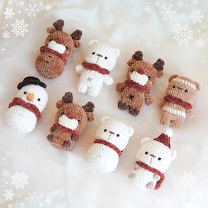 May include: Eight crocheted stuffed animals, including a snowman, reindeer, and polar bears, with brown and white fur and red scarves. The animals are arranged on a white background.