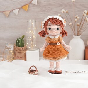 May include: A crocheted doll wearing a brown dress with a white collar and a white crocheted hat. The doll has brown hair and brown eyes. The doll is holding a small brown basket.