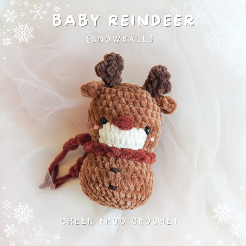May include: A brown crocheted reindeer toy with a white face and red nose. The toy is wearing a red scarf and has the text "BABY REINDEER (SNOWBALL)" above it and "GREEN FROG CROCHET" below it.