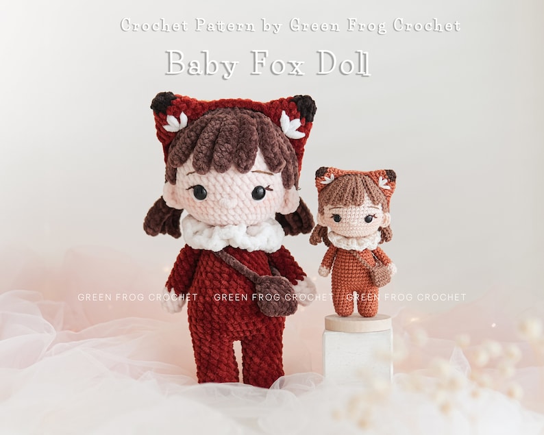 May include: Two crocheted fox dolls, one larger than the other, both wearing red and brown outfits with white accents. The dolls have brown hair and black eyes. The larger doll is holding a small brown bag. The dolls are sitting on a white surface with a pink background. Crochet Pattern by Green Frog Crochet Baby Fox Doll