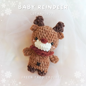 May include: A brown crocheted baby reindeer toy with a red nose and antlers. The reindeer is wearing a red scarf and is standing on a white background. The text "BABY REINDEER (STANDING)" is above the toy and the text "GREEN FROG CROCHET" is below the toy.