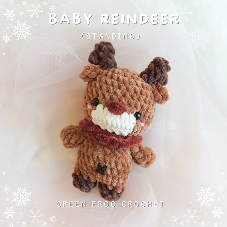 May include: A brown crocheted baby reindeer toy with a red nose and antlers. The reindeer is wearing a red scarf and is standing on a white background. The text "BABY REINDEER (STANDING)" is above the toy and the text "GREEN FROG CROCHET" is below the toy.