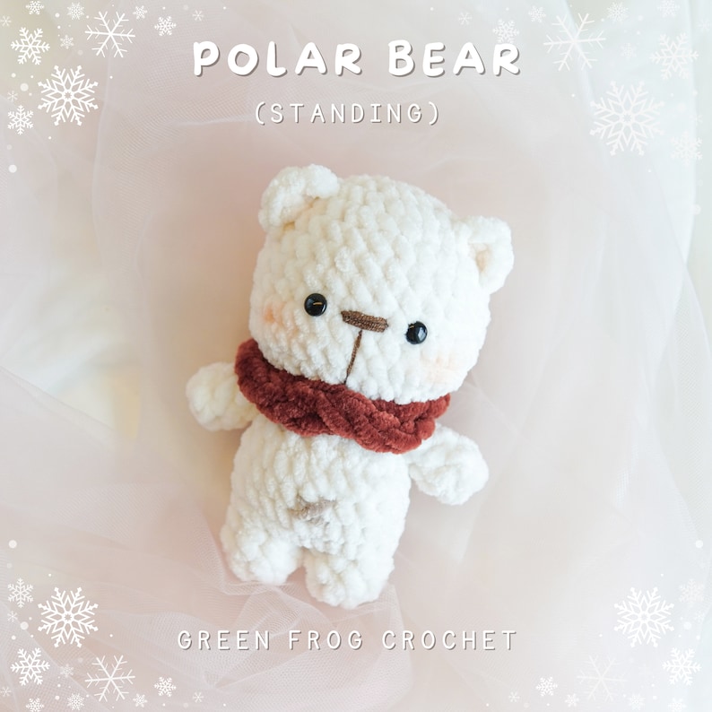 May include: White crocheted polar bear standing with a red scarf. The bear has black eyes and a brown nose. The background is a pink and white fabric with snowflakes.