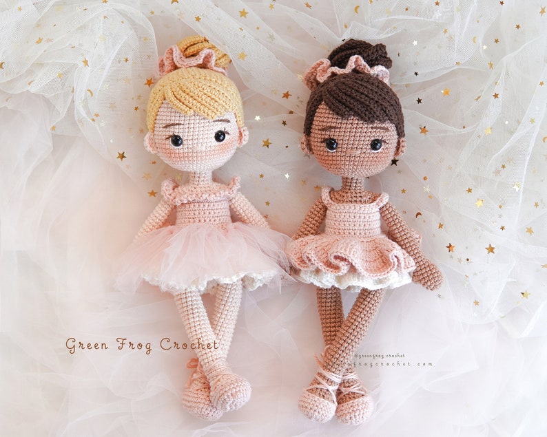 Puede incluir: Dos mu&ntilde;ecas de bailarina de crochet, una con cabello rubio y otra con cabello casta&ntilde;o, con tut&uacute;s rosas y zapatos de ballet blancos. Las mu&ntilde;ecas est&aacute;n colocadas sobre un fondo blanco con estrellas doradas brillantes.