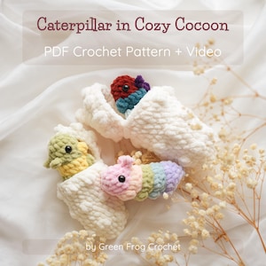May include: A close-up of three colourful, crocheted caterpillars nestled in white, fluffy cocoons. The caterpillars are in shades of green, pink, and rainbow colours. The text "Caterpillar in Cozy Cocoon" and "PDF Crochet Pattern + Video" is visible.
