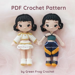 May include: Two crocheted dolls holding hands. One doll wears a white and gold outfit, the other a blue and yellow outfit. The dolls have black hair and are wearing earrings. The text "PDF Crochet Pattern" and "by Green Frog Crochet" are visible.