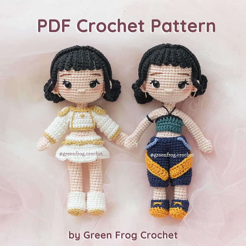 May include: Two crocheted dolls holding hands. One doll wears a white and gold outfit, the other a blue and yellow outfit. The dolls have black hair and are wearing earrings. The text "PDF Crochet Pattern" and "by Green Frog Crochet" are visible.