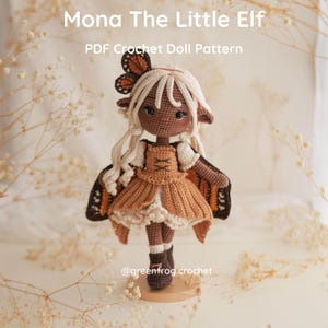 May include: A crochet doll named Mona The Little Elf with light hair, dark skin, and pointed ears. The doll wears a tan dress, brown boots, and butterfly wings. Text reads: Mona The Little Elf, PDF Crochet Doll Pattern, @greenfrog.crochet.