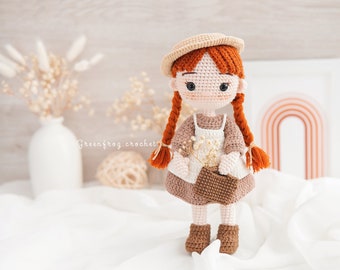 May include: A crocheted doll with brown hair, wearing a brown dress, a brown hat, and brown shoes. The doll is holding a small brown basket with white flowers.