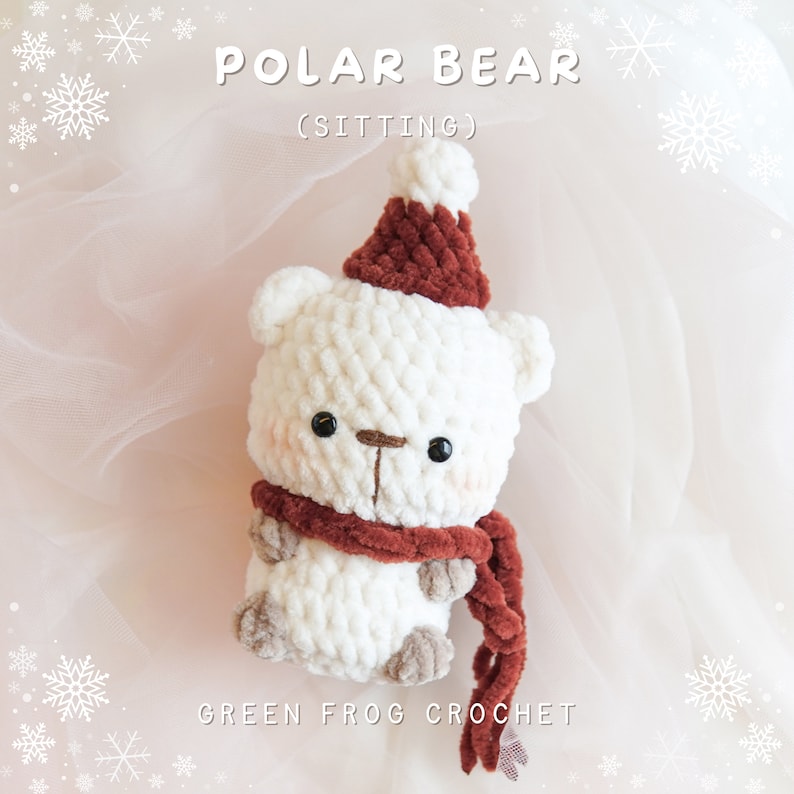 May include: White crocheted polar bear wearing a red crocheted hat and scarf. The bear is sitting and has black eyes and a brown nose. The text "POLAR BEAR (SITTING)" is above the bear and the text "GREEN FROG CROCHET" is below the bear.
