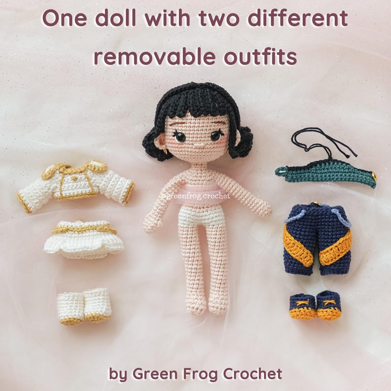 May include: A crocheted doll with black hair and two sets of removable outfits. One outfit is white with gold trim, and the other is navy blue with yellow accents. The doll is standing next to the outfits. Text on the image reads "One doll with two different removable outfits" and "by Green Frog Crochet."