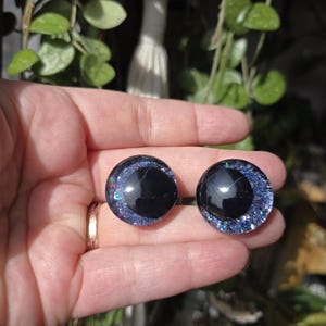 May include: Two black and blue round googly eyes with glitter accents. The eyes are about 1 inch in diameter.