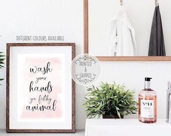 Puede incluir: Una impresión enmarcada con el texto "Wash your hands ya filthy animal" en escritura negra sobre un lavado de acuarela rosa. El marco es de color marrón oscuro. Las palabras "Diferentes colores disponibles" están encima del marco.
