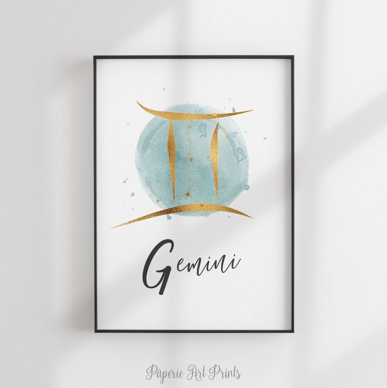May include: A watercolor print featuring the Gemini zodiac sign in gold with a blue watercolor background. The word "Gemini" is written in black below the sign.
