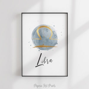May include: A watercolor print of the Libra zodiac sign in gold on a blue background. The word "Libra" is written in black cursive below the sign.