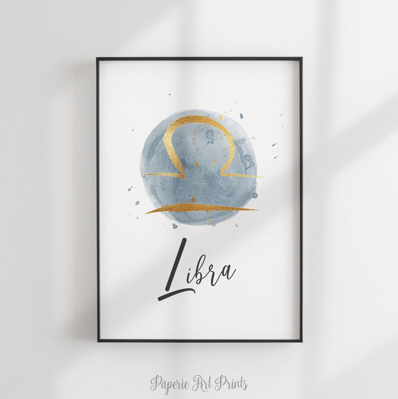 May include: A watercolor print of the Libra zodiac sign in gold on a blue background. The word "Libra" is written in black cursive below the sign.