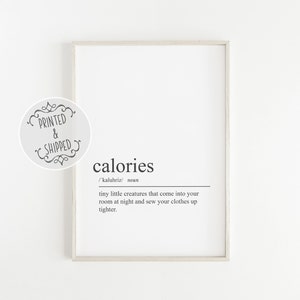 Op de afbeelding: Een wit ingelijst print met een zwart-witte definitie van het woord "calorieën". De definitie luidt: "/'kaluhriz/ zelfstandig naamwoord kleine wezentjes die 's nachts je kamer binnenkomen en je kleren strakker naaien."